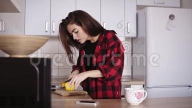 年轻漂亮的女孩穿着红法兰绒衬衫，切柠檬，然后在厨房里给自己泡了一杯茶。